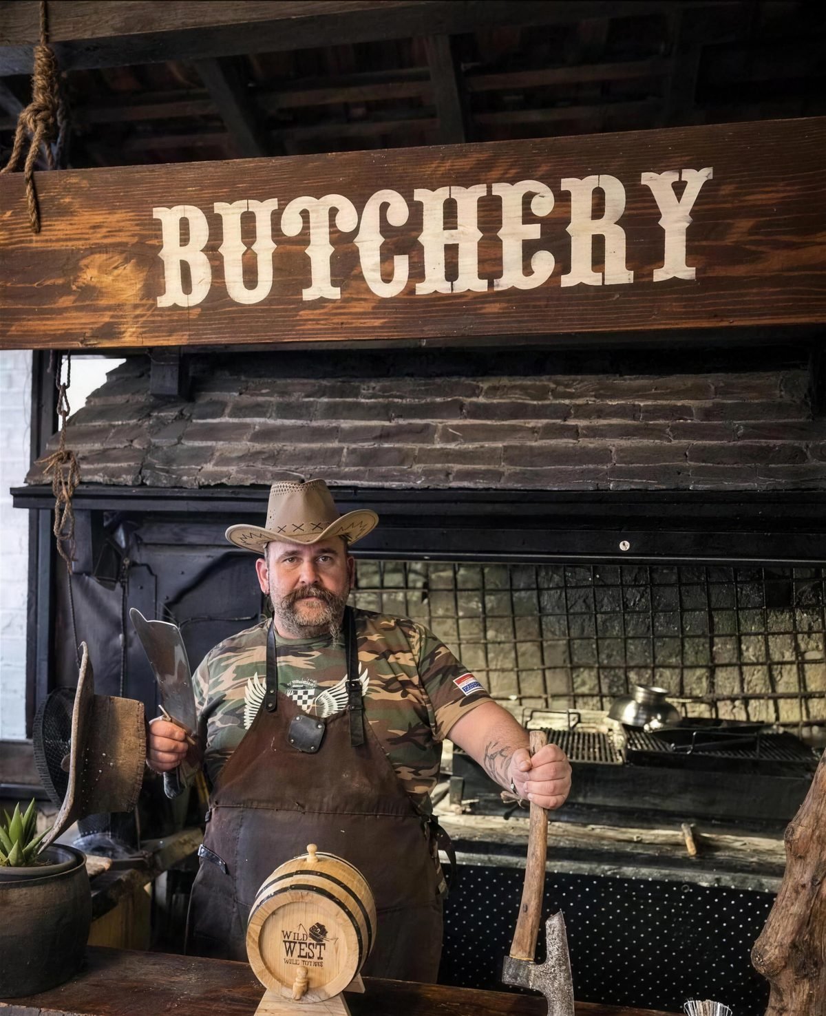 Grill master in a cowboy hat and leather apron in front of the open charcoal grill